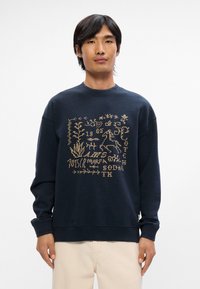 Σκούφος ναυτικού χρώματος με υφή και κεντημένο σχέδιο σε μπεζ, που απεικονίζει φυτά και έναν άλογο, διαθέτει στρογγυλή λαιμόκοψη και ριγέ μανίκια.