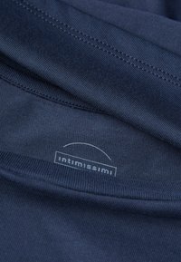 Námořnická modrá látka s jemným žebrováním, na které je viditelná značka s logem "intimissimi". Bezešvé okraje a měkká textura jsou patrné na záhybech.