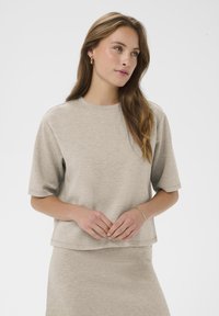 Bežs īsām piedurknēm tops, kas izgatavots no mīksta auduma ar brīvu piegriezumu un apaļu izgriezumu. Izceļas ar taisnu apdari un smalku tekstūru visā virsma.