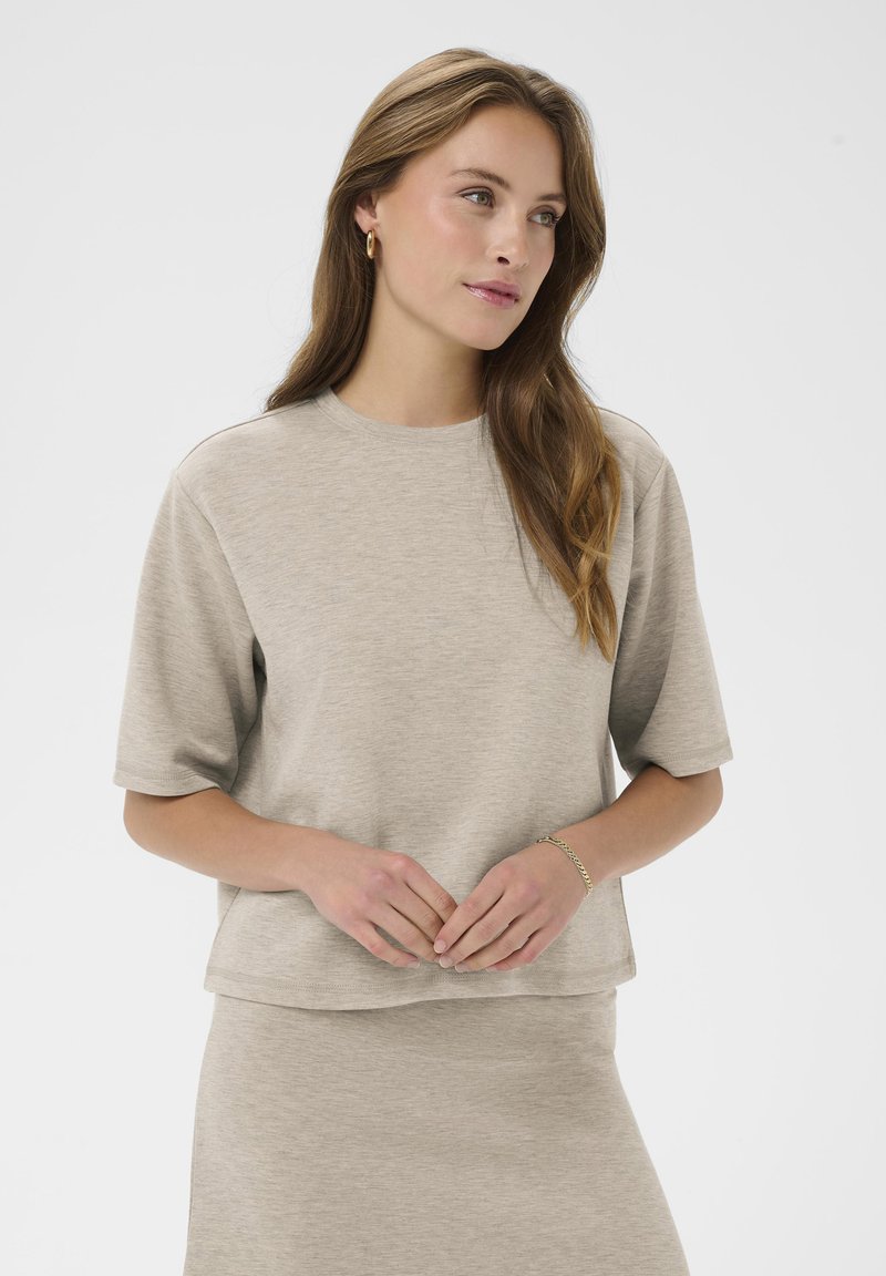 Bežs īsām piedurknēm tops, kas izgatavots no mīksta auduma ar brīvu piegriezumu un apaļu izgriezumu. Izceļas ar taisnu apdari un smalku tekstūru visā virsma.