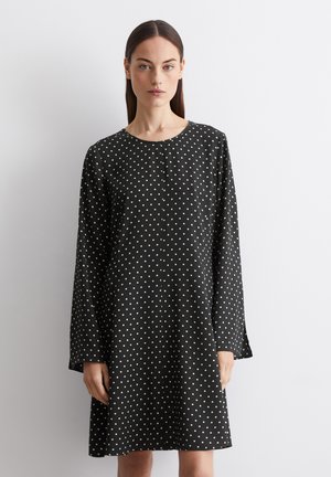 Robe noire à manches longues et décolleté rond, présentant un motif à pois blancs et une silhouette droite. Texture de tissu lisse.