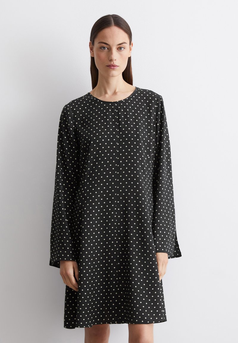 Robe noire à manches longues et décolleté rond, présentant un motif à pois blancs et une silhouette droite. Texture de tissu lisse.