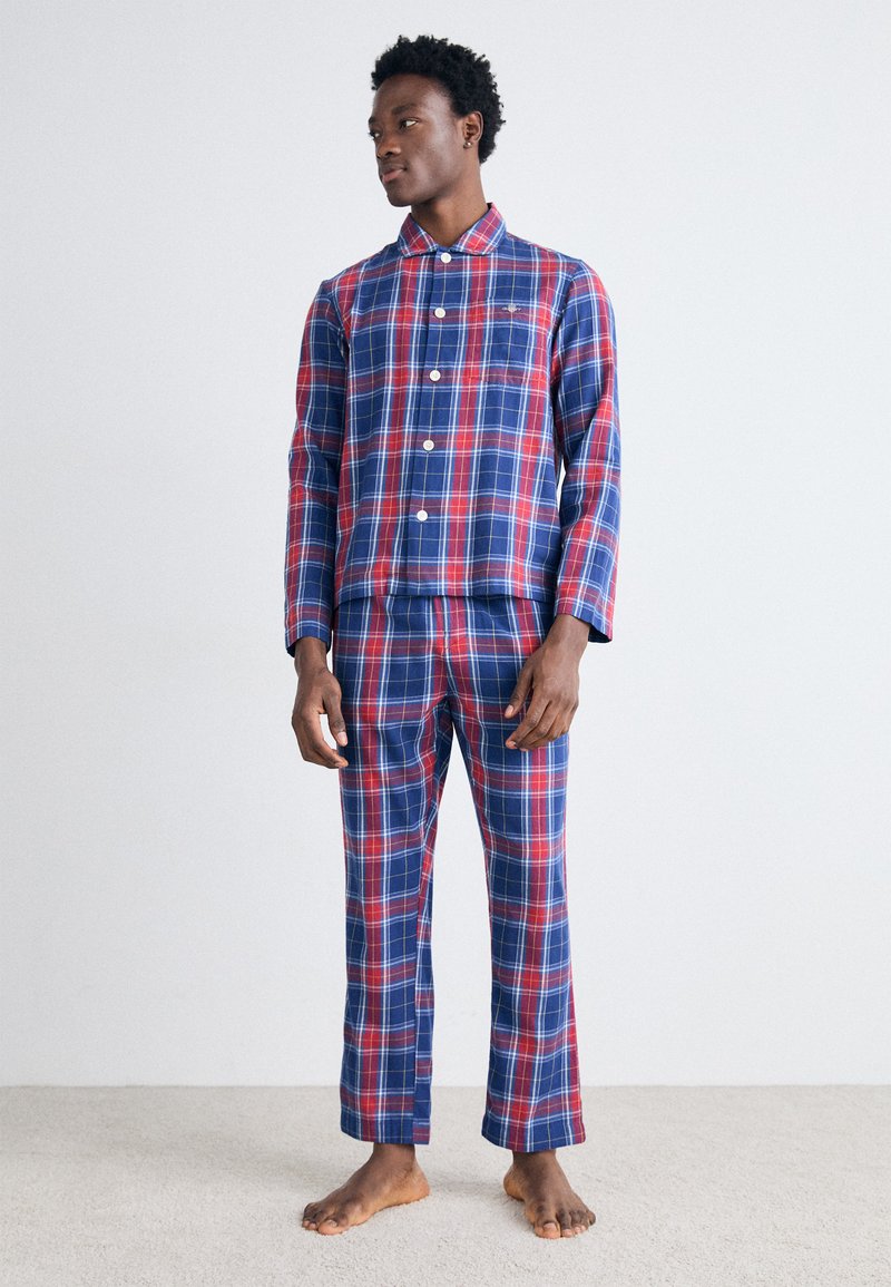 Conjunto de pijama de cuadros en azul, rojo y blanco. Parte superior de manga larga con cuello y cierre de botones, pantalones a juego con pierna recta. Textura de tela suave.