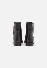 Bottines en cuir noir avec une finition lisse, des panneaux latéraux en élasthanne et un accent métallique. Le design présente un talon bas et une forme structurée.