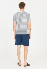 Gestreepte witte en marineblauwe t-shirt met korte mouwen; gecombineerd met effen marineblauwe shorts. Casual pasvorm, zachte textuur en bruine instappers.