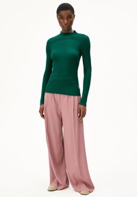 Groene geribbelde langemouwen top met een hoge halslijn, gecombineerd met losse, lichtroze broeken. De stof lijkt glad en zacht te zijn.
