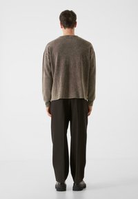 Suéter marrón de punto con un corte holgado, mangas largas y cuello redondo, combinado con pantalones negros sueltos y zapatos negros de plataforma.