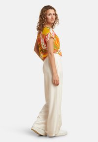 Kleurige korte mouwen top met bloemmotieven in geel, roze en groen, gecombineerd met hoge witte wijde broek en witte sneakers.