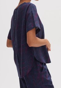 Kort navyblauw blouse met korte mouwen en een gestructureerd patroon van verticale lijnen in paars en roze. Heeft knopen aan de achterkant en een afgeronde zoom.