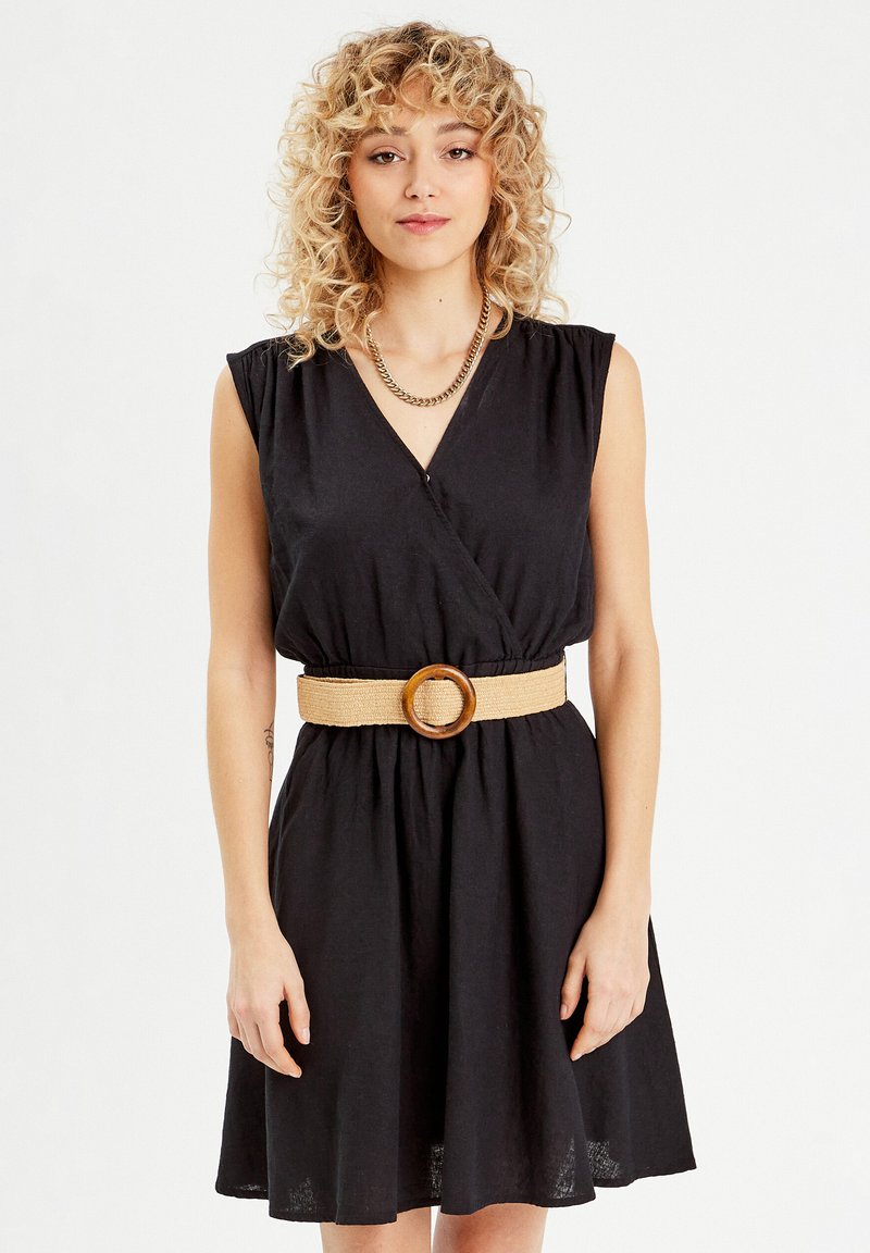 Abito nero avvolgente con maniche corte e vita cinchata, dotato di una cintura intrecciata color crema con un anello di legno. Tessuto liscio, lunghezza al ginocchio.