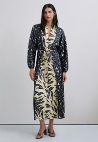 Vestido largo estilo envolvente en negro y beige, con estampados de animales, cinturón en la cintura y mangas abullonadas. Textura de tela suave.