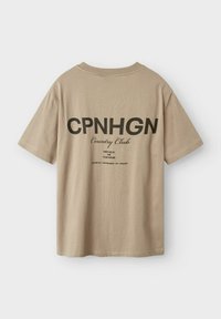 Beež lühikeste varrukatega T-särk, mille seljal on must graafiline tekst, sealhulgas "CPNHGN Country Club" ja täiendavad üksikasjad all.