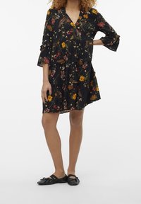 Blommig svart klänning med V-urringning, 3/4 ärmar, lager på lager kjol och färgglada blomster mönster. Bärs med svarta platta skor.