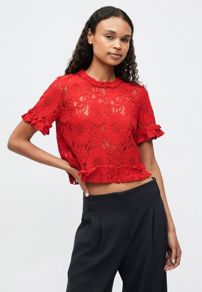 Červený krajkový crop top s květinovými vzory, volánkovými rukávy a volánkovým lemem. Slaďený s tmavými kalhotami s vysokým pasem.