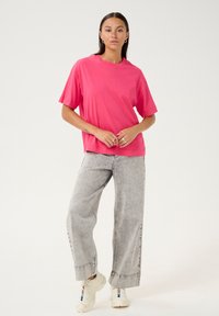 Lyserød bomulds t-shirt med korte ærmer, afslappet pasform, parret med lys grå brede jeans og hvide sneakers. Enkel, moderne design.