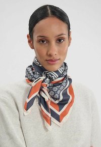 Foulard en soie avec une base bleu marine et des motifs géométriques en bleu clair et orange, noué soigneusement autour du cou.