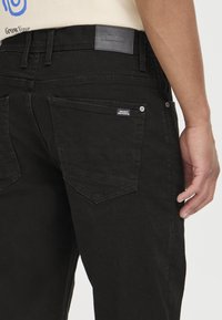 Jeans de mezclilla negra con corte ajustado, que presentan dos bolsillos traseros, una etiqueta de cuero con marca y costuras en contraste a lo largo de las costuras.