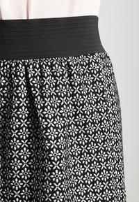 Schwarz-weiß gemusterter Rock mit floralen Motiven und einem breiten, strukturierten schwarzen Bund, der ein gerafftes Design für eine lockere Passform aufweist.