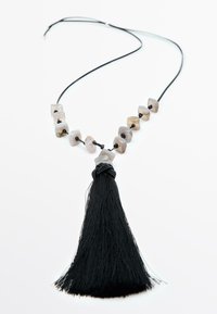Collier avec un pompon noir et des perles à motifs géométriques dans des nuances de gris et de beige, enfilé sur un fin cordon noir.