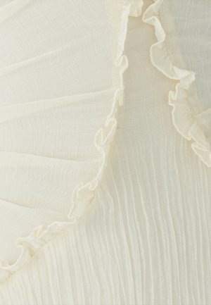 Tela de marfil claro con delicados volantes en uno de sus bordes, con una superficie texturada y plisada que muestra sutiles líneas horizontales.