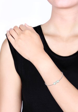 Silver chain bracelet with three turquoise stones, worn on a bare arm, against a black sleeveless top and neutral background.