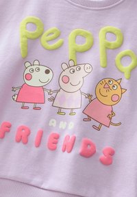Svetlo vijoličasta majica s kapuco z barvitimi, dvignjenimi grafikami treh risanih junakov in velikim besedilom, ki pravi "Peppa in prijatelji."