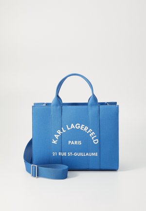 Niebieska prostokątna torba typu tote z krótkimi uchwytami i regulowanym paskiem na ramię, z nadrukiem "Karl Lagerfeld Paris 21 Rue St-Guillaume" białymi literami.