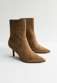 Bottines en suède tan avec un bout pointu, un talon aiguille slim et un design épuré ; texture douce avec une finition soignée.