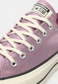 Gros plan d'une basket Converse All Star rose avec des lacets blancs et une semelle de couleur crème.