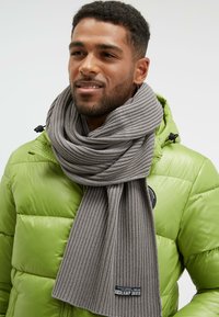 Gray ribbed scarf wrapped around the neck, paired with a vibrant green puffer jacket. Tag visible at the scarf's end.
