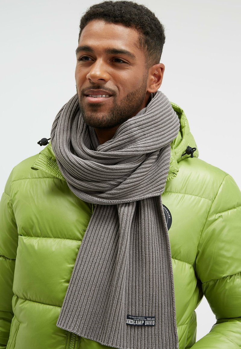 Gray ribbed scarf wrapped around the neck, paired with a vibrant green puffer jacket. Tag visible at the scarf's end.