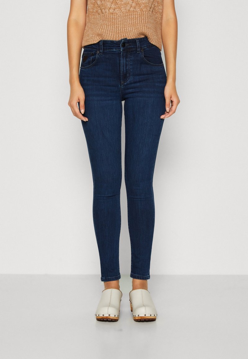 Hubené modré džíny s vysokým pasem, které mají dvě přední kapsy a hladkou texturu. Kombinované se světlými dřeváky.