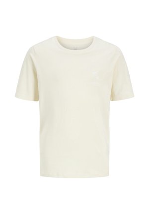 Niño con gorra verde, camiseta blanca texturizada de manga corta sobre camiseta crema, pantalones cortos negros, calcetines blancos y zapatillas blancas, de pie.