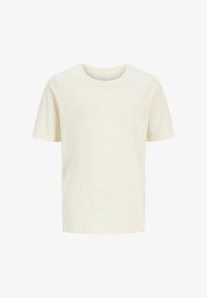 Niño con gorra verde, camiseta blanca texturizada de manga corta sobre camiseta crema, pantalones cortos negros, calcetines blancos y zapatillas blancas, de pie.