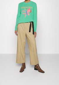 Mintgroene trui met de tekst "WEEKENDERS" en een vlinderontwerp, gecombineerd met beige wijde broek en bruine haklaarsjes.
