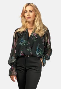 Czarna bluzka w kwiaty z przezroczystego materiału, z kolorowymi wzorami w niebieskim, różowym i zielonym kolorze. Luzny krój z elastycznymi mankietami i dekoltem w serek.