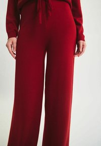 Pantalons larges rouges en tissu tricoté texturé, dotés d'une taille élastique avec un cordon de serrage pour un ajustement réglable.