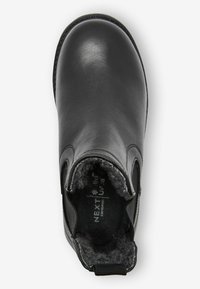 Svart läderankle stövel med elastiska sidor, mjukt foder i päls, rundad tå och dragflik baktill; texturerad grå inredning.