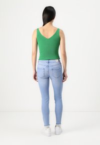 Green ribbed tank top with a V-back, paired with light blue skinny jeans, and white sneakers. Smooth fabric, fitted design, and minimal details.