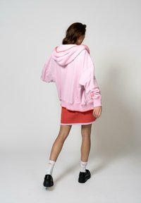 Felpa oversized rosa con un bordo arancione a contrasto, abbinata a una gonna corallo. Scarpe con plateau nere e calze bianche completano l'outfit.