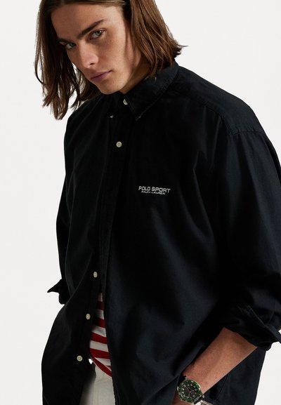 Camisa negra de botones con cuello apuntado, logo bordado de "Polo Sport" en el pecho izquierdo y un corte relajado.