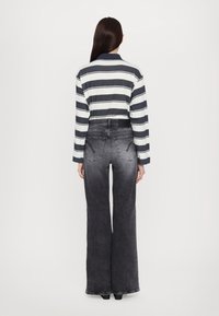 Maglietta a maniche lunghe a righe in blu navy e bianco, abbinata a jeans neri a vita alta e gamba larga con effetto sbiadito e tasche posteriori.