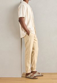 Lichtbeige gestreept shirt met korte mouwen, beige linnen tapered broek en grijze sandalen met verstelbare band. Gladde textuur, casual pasvorm.