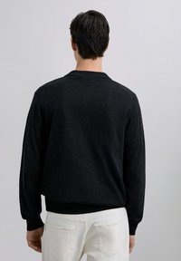 Suéter negro de punto con cuello redondo, puños y dobladillo acanalados. Textura suave, corte ligeramente relajado, visto desde la parte posterior sobre un fondo claro.