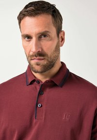 Bordeauxfarbendes Poloshirt aus strukturiertem Stoff, mit einem Umlegekragen, einer Drei-Knopf-Leiste und navyfarbenen Akzentnähten. Gesticktes Logo.