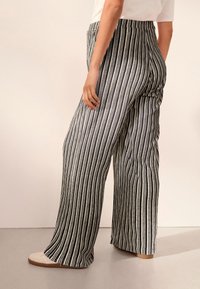 Pantaloni a gamba larga con righe verticali bianche e nere; cintura elastica, tessuto morbido e vestibilità rilassata; abbinati a calzature chiare.