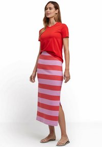 Rode t-shirt met korte mouwen gecombineerd met een midi-rok in roze en rode strepen met splitten aan de zijkanten en platte sandalen.