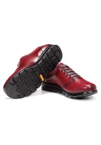 Chaussures en cuir rouge avec des lacets gris, bout arrondi et semelle en caoutchouc noir texturé avec un motif antidérapant et un accent orange au niveau du talon.