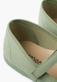 Zapatillas de lona verdes con un acabado texturizado, que cuentan con un interior suave y una suela plana y flexible. Incluyen un diseño de correa para un ajuste seguro.