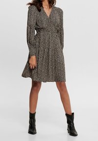 Schwarzes Blumen-Wickelkleid mit langen Ärmeln, schwingendem Rock und V-Ausschnitt. Aus leichtem Stoff gefertigt, mit kleinen weißen und beigen Blumen.